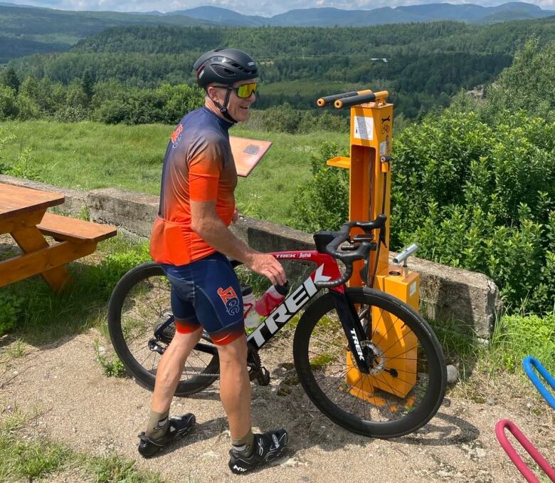 A man wearing biking clothes and a helmet, standing next to a mountain bike.