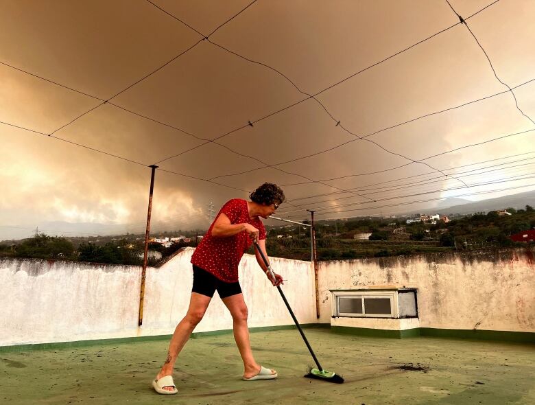 Josefina Minguillon, 62, sweeps the ash off the terrace of her house while smoke rises over the village of Benijos in Tenerife on Saturday.