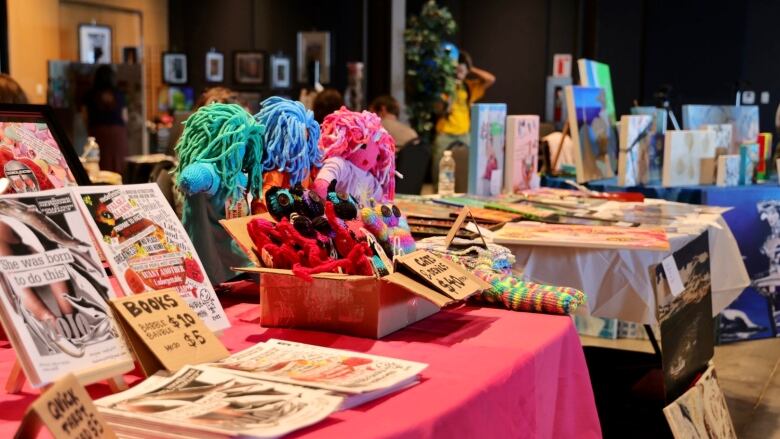 Three tables are lined up with different artists work displayed on each one. 