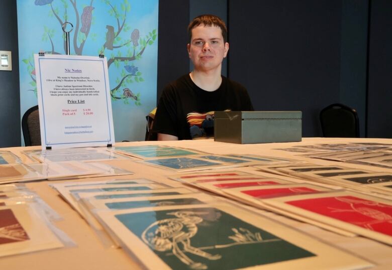 Nicholas sits at a table with several of his drawings on display. 