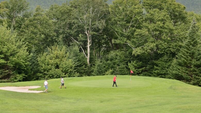 Three golfers walk onto a green at Indian Lake Golf Course. 