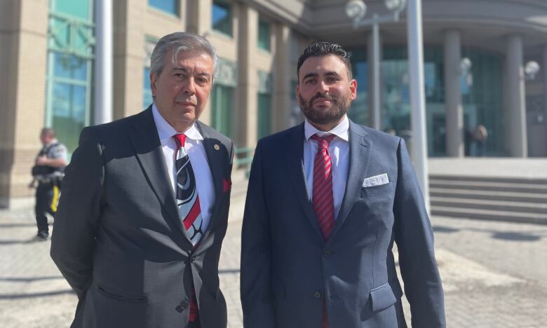 Two lawyers in suits and tie look serious as they stand in front of the courthouse in Prince George. 