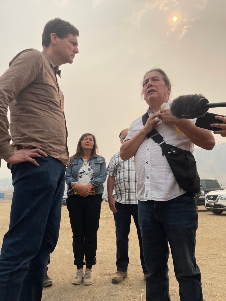 Two men stand together in a dusty field speaking.