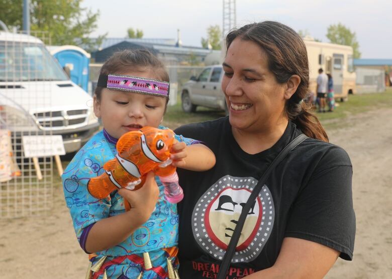 A First Nations woman and her granddaughter smile while the child plays with a toy.