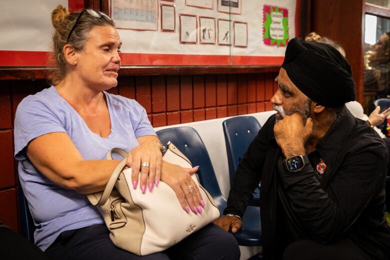 A woman wearing purple talks to a man who is kneeling on the floor to listen to her.