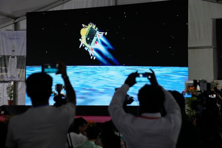 People taking photos of a satellite on a large screen in front of them. 