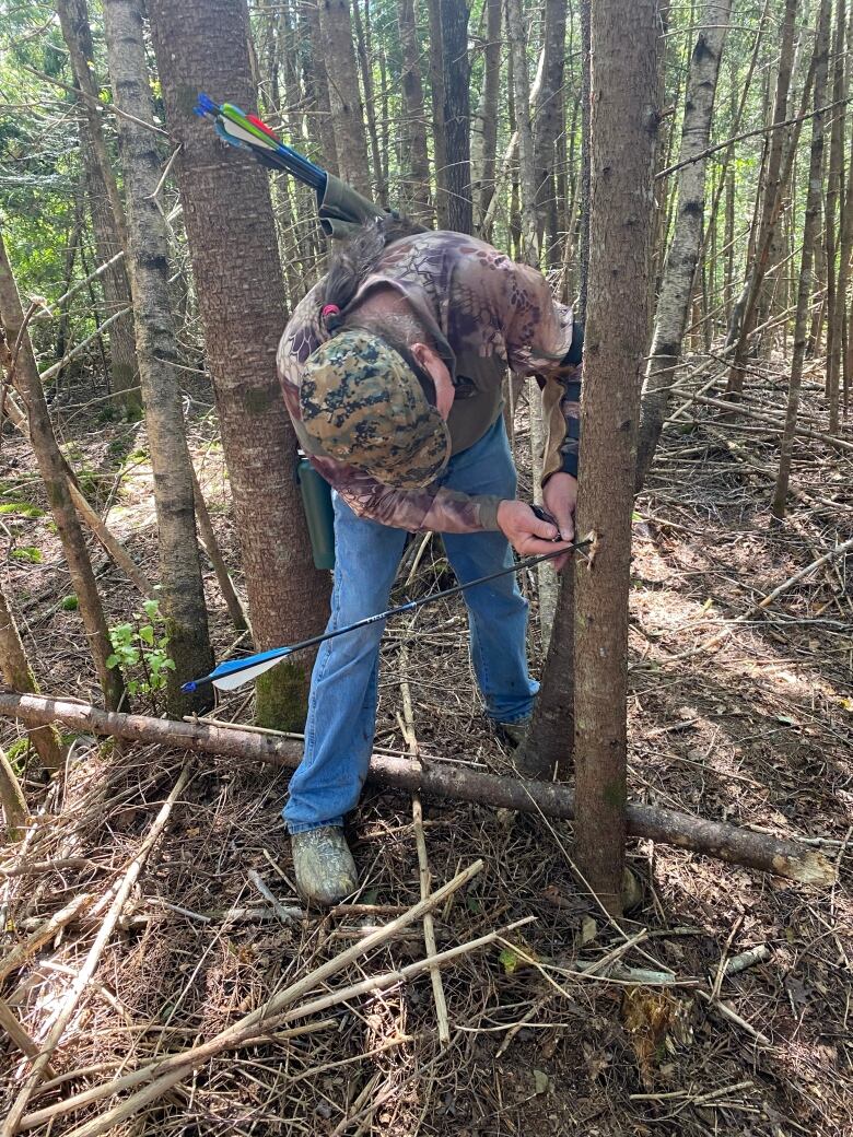 man taking out arrow pierced through a tree in the woods