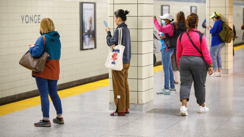 Commuters are photographed on their phones at Yonge Station in Toronto on Aug. 23, 2023. 