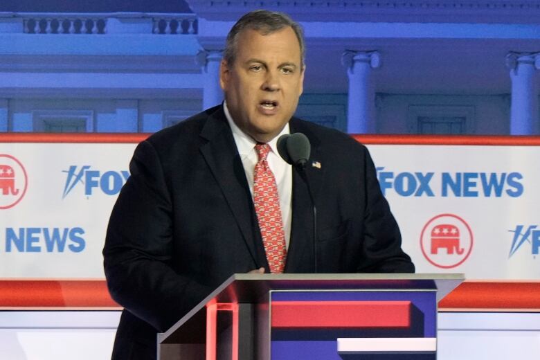 Man in dark suit and red tie speaking at a podium