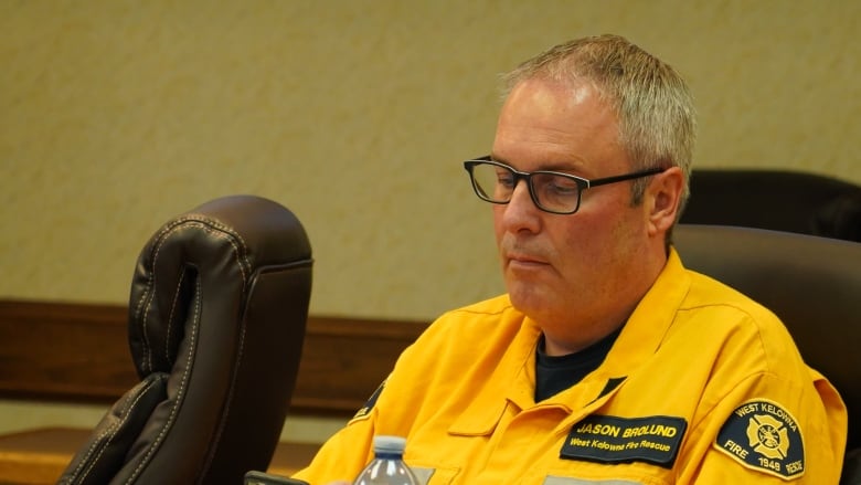 A white man wearing a yellow uniform looks down at his phone.