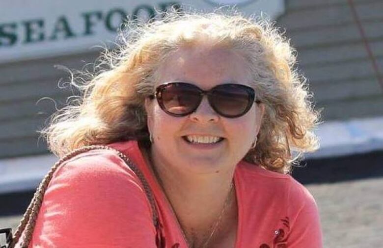 A woman in sunglasses and a pink shirt smiles.