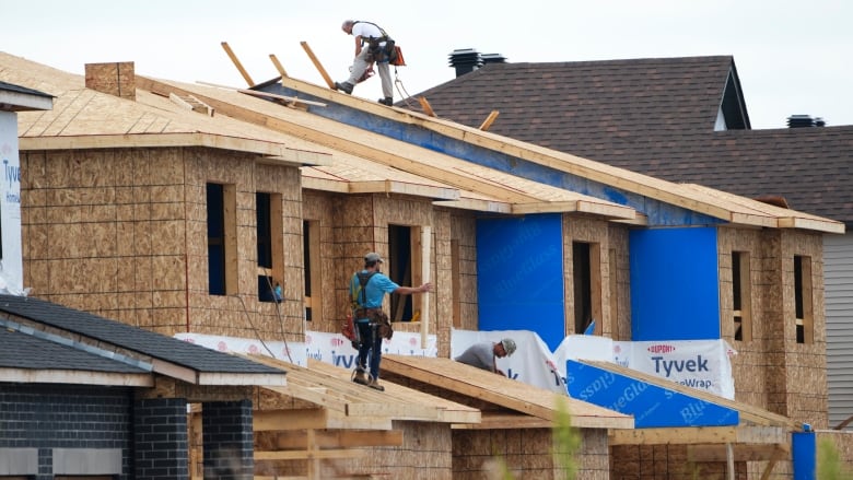 An image of two construction workers standing on the roofs on a string of houses being built.