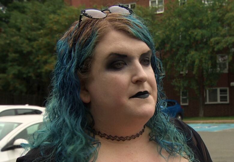 A woman with blue hair standing in a parking lot. 