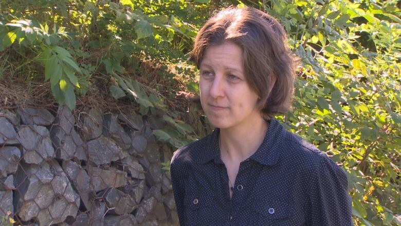 A woman in a blue shirt is pictured in front of a wall with foliage.