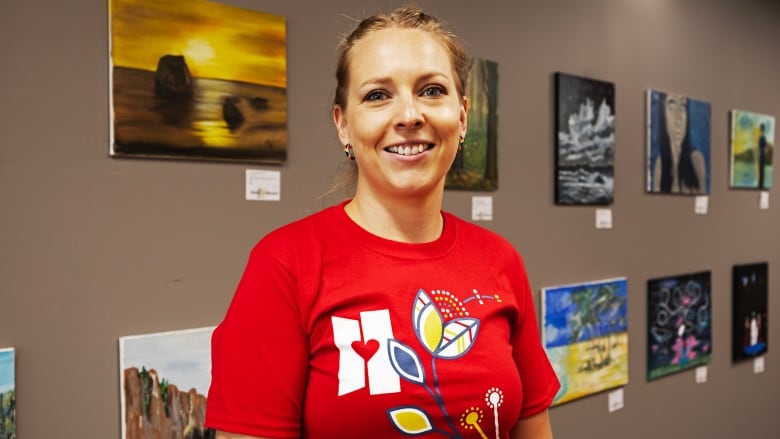 A woman stands in front of a wall with paintings hanging from it.