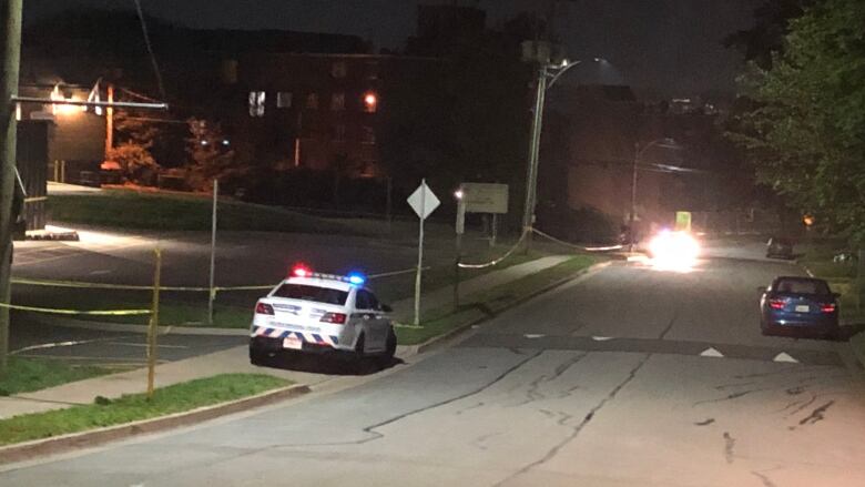 A police car is seen on a dark, empty street beside a single storey school building. There's caution tape along the sidewalk.