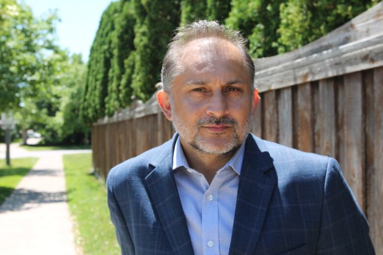 A man in a suit jacket looks into the camera on a residential street