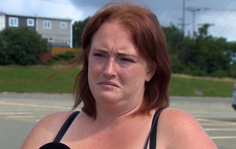 A woman with red hair stands in a mall parking lot.