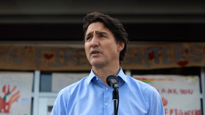 Prime Minister Justin Trudeau, wearing a blue collared shirt, speaks at a microhpone.