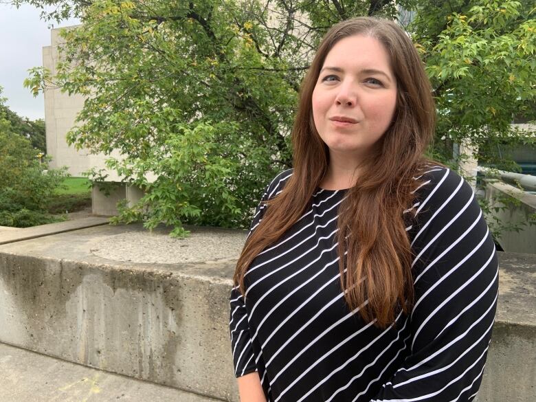 A brunette woman in a striped shirt outside in from of a concrete building. 