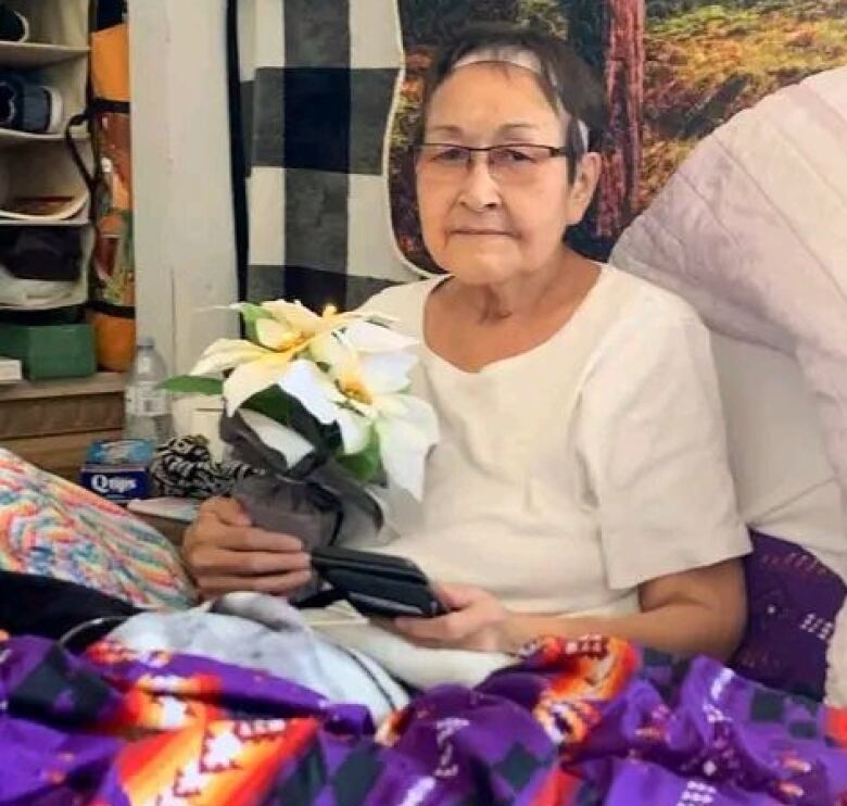 An elder holds a flower pot while covered in a blanket. 