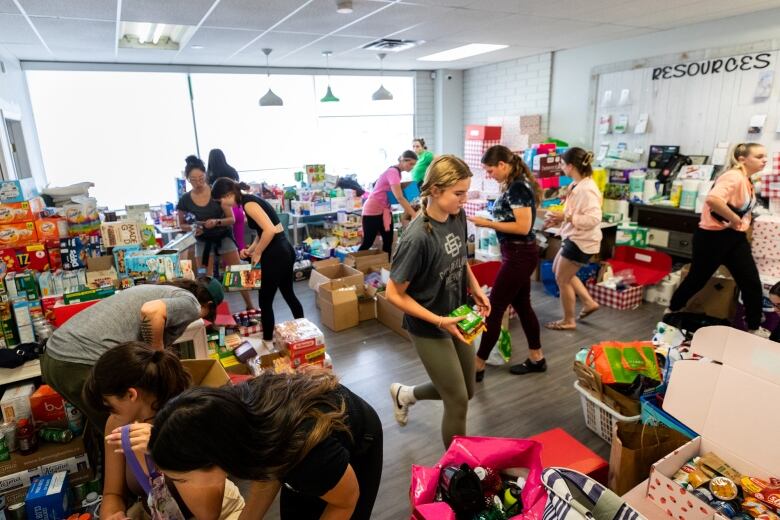 A large room full of supplies with 10 or so people sorting food and clothing.