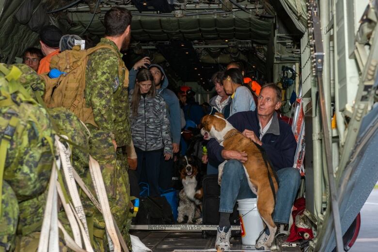 People in military gear gather with a bunch of other people and dogs inside a big aircraft.