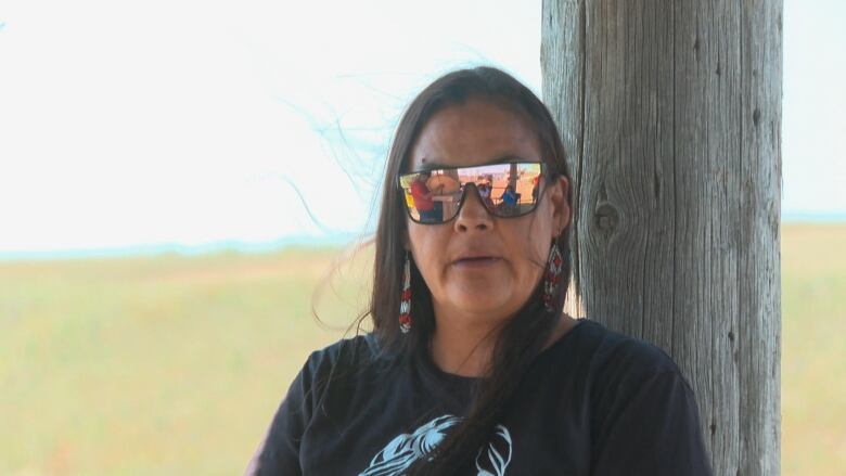 A woman with long black hair looks at the camera. She is wearing reflective sunglasses. 