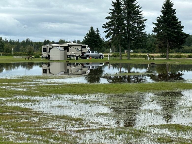 A swampy area of a park is seen in the foreground with an RV and pickup truck in the middle distance.