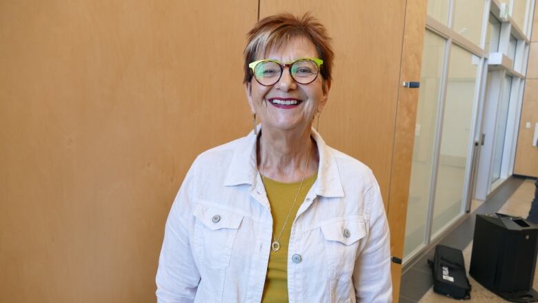 A woman wearing glasses stands next to a wooden wall.