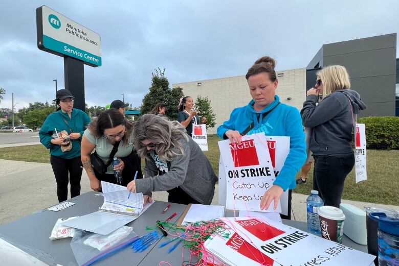 A group of people stand near a table where there is a clipboard and stack of strike signs