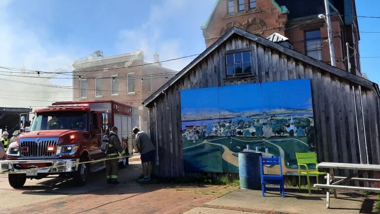 Two buildings and a fire truck are shown, with smoke in the air.