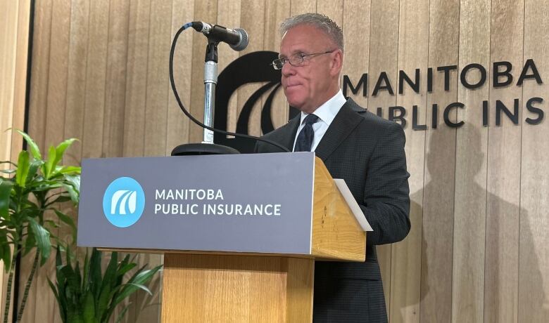 A man with short hair stands at a podium, wearing a suit.