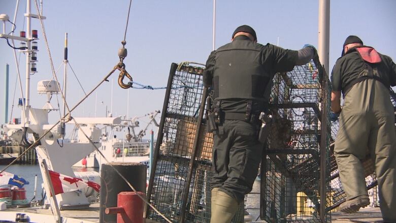 A man stands behind two large lobster traps.