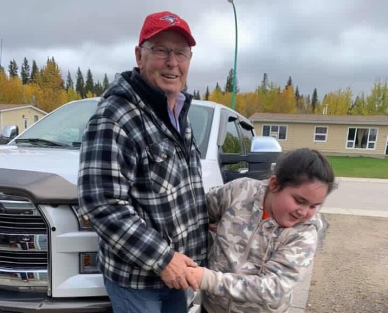 An elderly man stands on a driveway holding hands with a young girl.