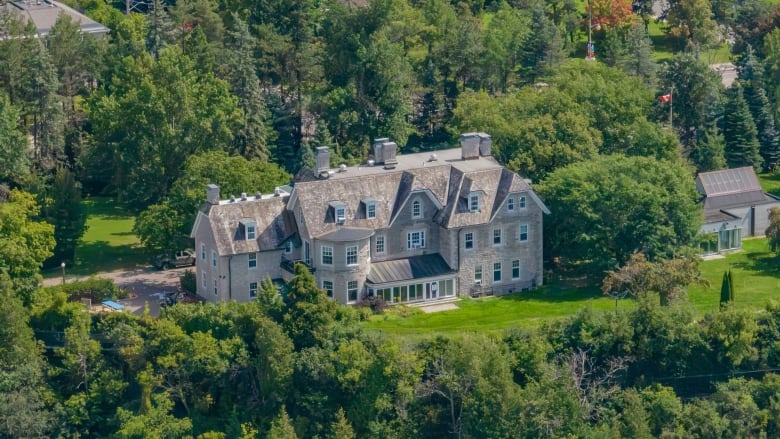 An aerial drone image of the prime minister's official residence in Ottawa with green lawn and surrounding trees.