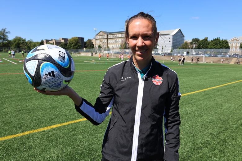 A soccer ref wearing black is showing the official World Cup ball used in the game between Denmark and China.