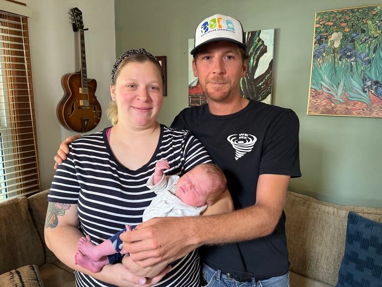 The mother and father of a newborn baby hold their daughter in their home.