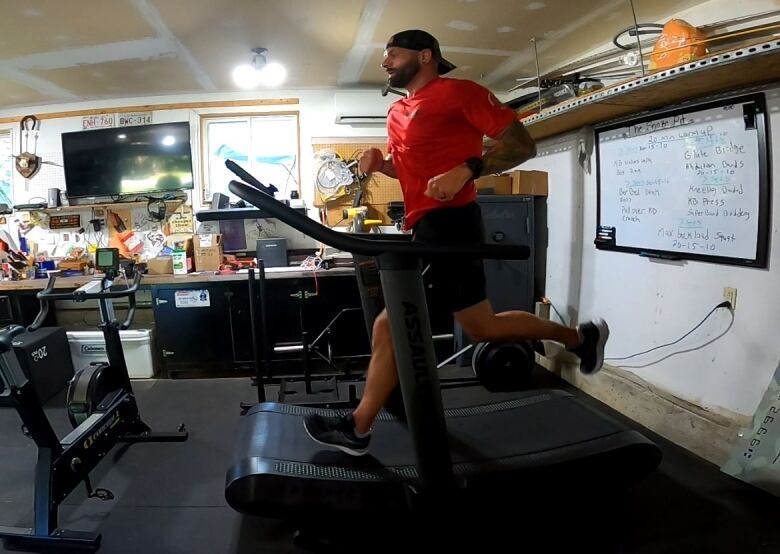 A bearded man in a red shirt and shorts runs on a treadmill.