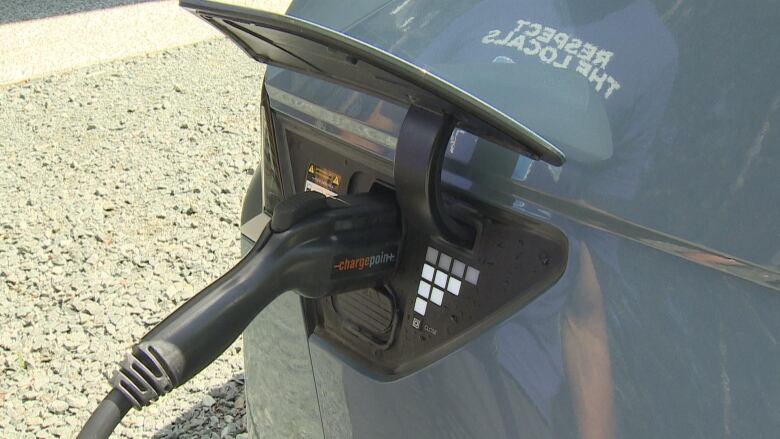 A Level 2 charger is seen plugged in to a grey vehicle's charging port.