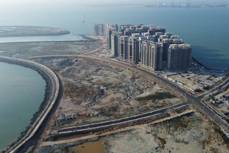 An aerial view shows a tight cluster of high-rise buildings on an otherwise largely undeveloped seaside. 