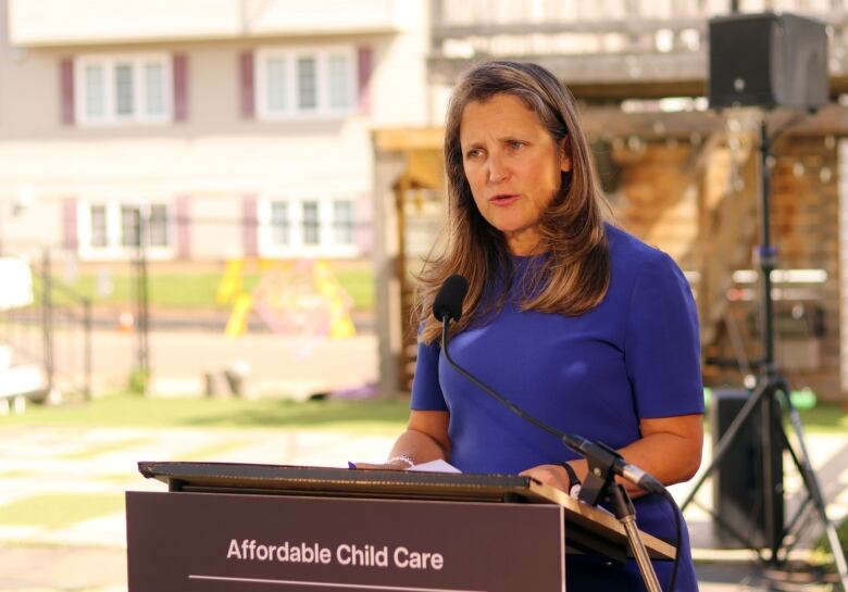 A woman in a blue dress speaks at a podium.