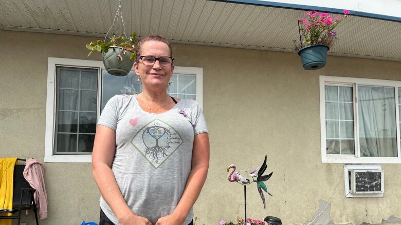 A woman in glasses stands in front of motel room, decorated with colourful statues and planters.