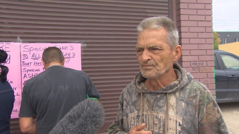 A man in a camouflaged hoodie speaks with media.