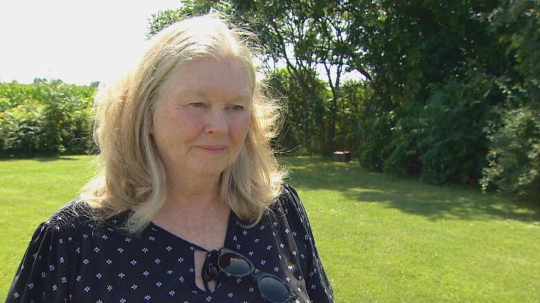 A woman conducts an interview in front of a farm field.