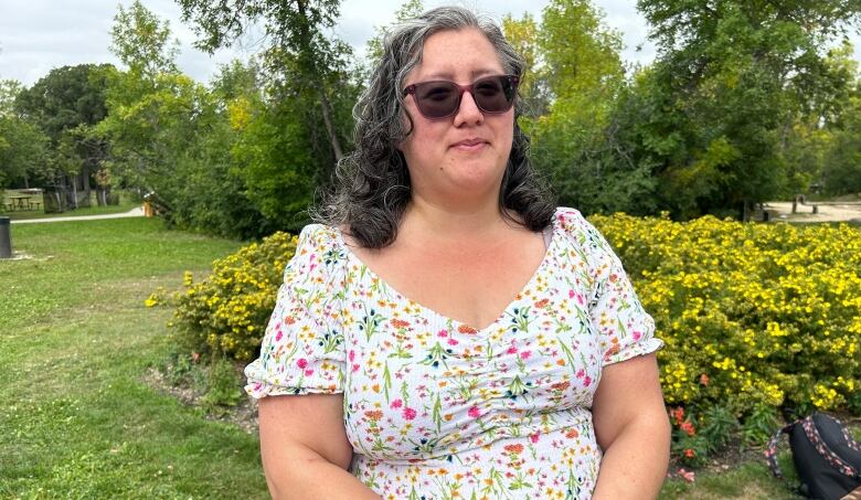 A woman in floral pattern shirt poses is pictured in front of a greenspace.