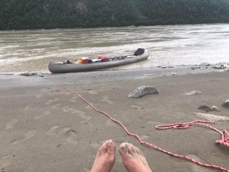 feet on the beach with a canoe and the Yukon River in the background.