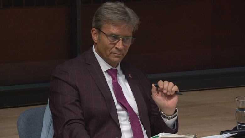 A man in a purplse suit holds a pen.