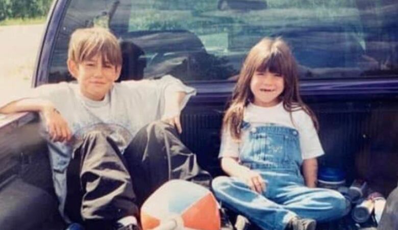 Two kids sit in the back of a pickup truck. 