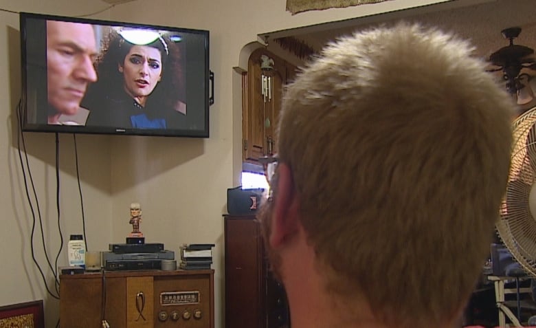 A man watches Counselor Troi from Star Trek on a wall-mounted TV.